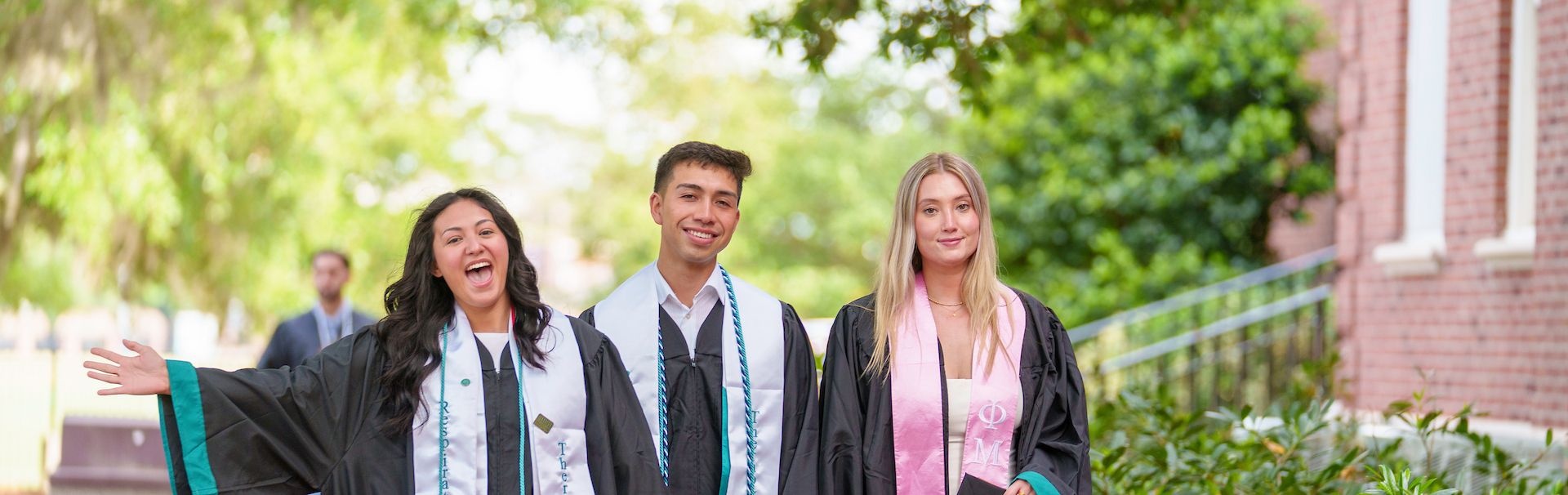 Three students walk outside to commencement together with the 'Respiratory Therapy' sashes and cords.
